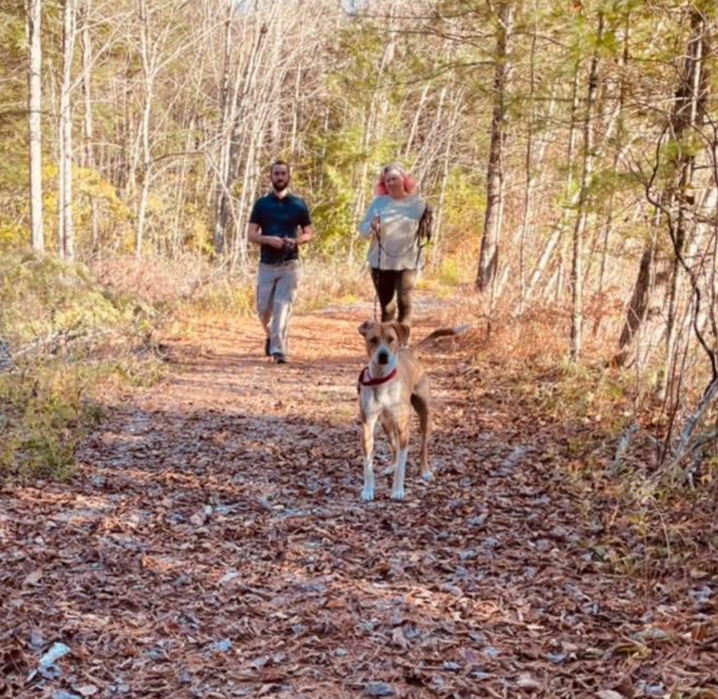 Trainer working with client and their dog on a trail in the fall